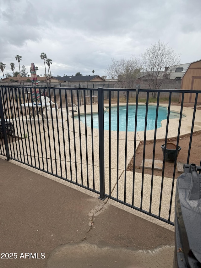 community pool featuring a storage shed, a patio area, fence, and an outbuilding