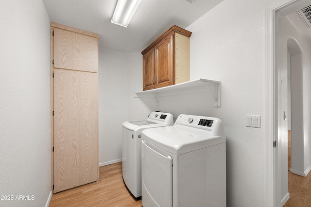 laundry area featuring washer and clothes dryer, cabinets, and light hardwood / wood-style flooring