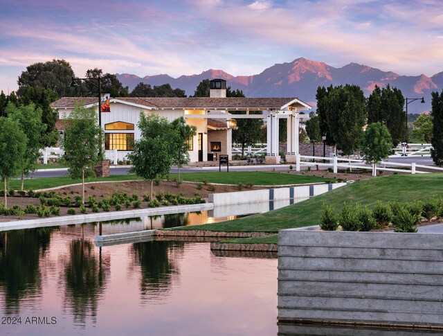 back house at dusk with an outdoor fireplace, a yard, and a water and mountain view