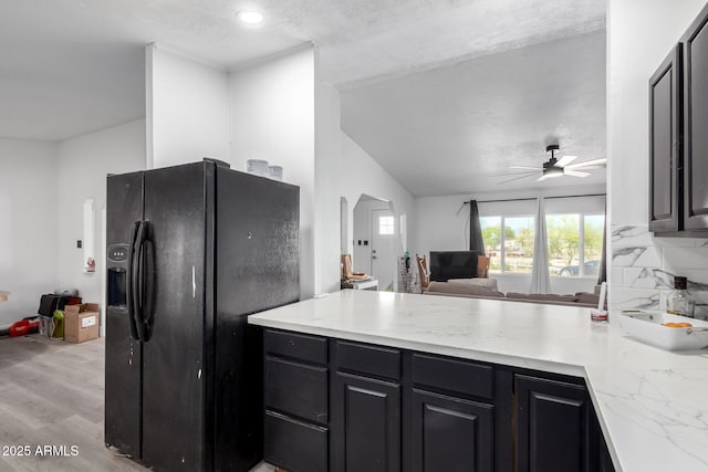 kitchen with ceiling fan, a peninsula, black refrigerator with ice dispenser, open floor plan, and light wood-style flooring