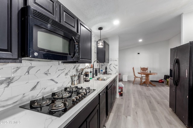 kitchen with a sink, dark cabinetry, tasteful backsplash, pendant lighting, and black appliances
