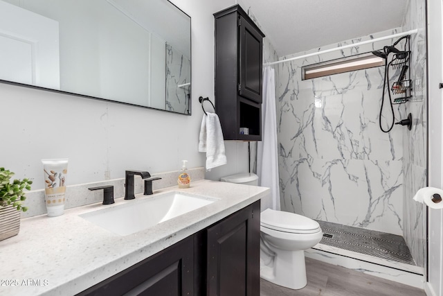 bathroom featuring vanity, a marble finish shower, wood finished floors, and toilet