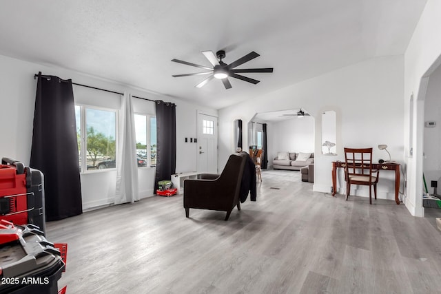 living area with arched walkways, ceiling fan, wood finished floors, and vaulted ceiling