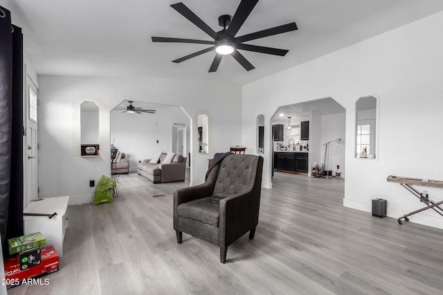 living room with arched walkways, ceiling fan, baseboards, and wood finished floors