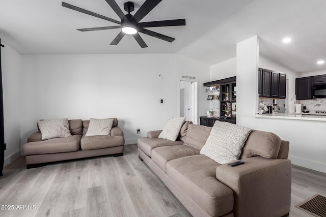 living area featuring ceiling fan, vaulted ceiling, baseboards, and light wood finished floors