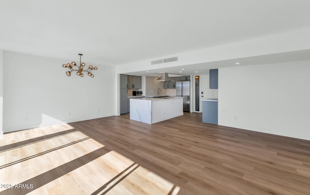 unfurnished living room with sink, a notable chandelier, and light wood-type flooring