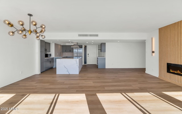 kitchen with an inviting chandelier, gray cabinets, stainless steel appliances, a large fireplace, and light hardwood / wood-style flooring