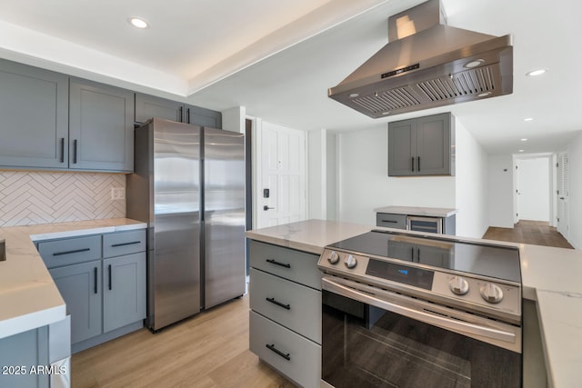 kitchen with tasteful backsplash, light hardwood / wood-style floors, island exhaust hood, light stone countertops, and appliances with stainless steel finishes