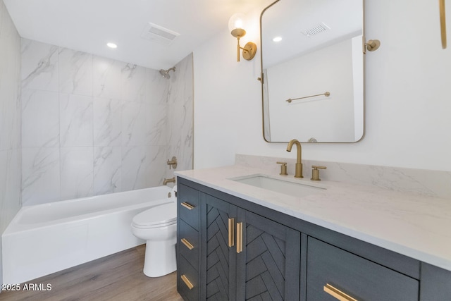 full bathroom with toilet, tiled shower / bath, vanity, and hardwood / wood-style floors