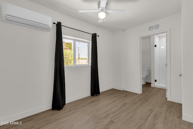 unfurnished bedroom featuring connected bathroom, ceiling fan, a wall mounted air conditioner, and light wood-type flooring