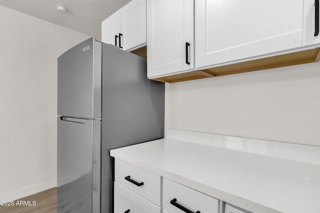 kitchen featuring stainless steel fridge, light hardwood / wood-style flooring, and white cabinets