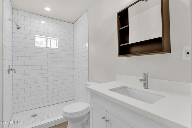 bathroom featuring a tile shower, vanity, and toilet