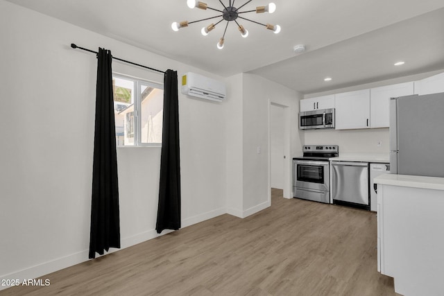 kitchen featuring light wood-type flooring, stainless steel appliances, a wall unit AC, an inviting chandelier, and white cabinetry