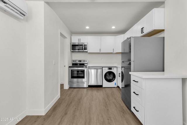 kitchen with stainless steel appliances, light hardwood / wood-style flooring, washer / clothes dryer, a wall mounted AC, and white cabinets