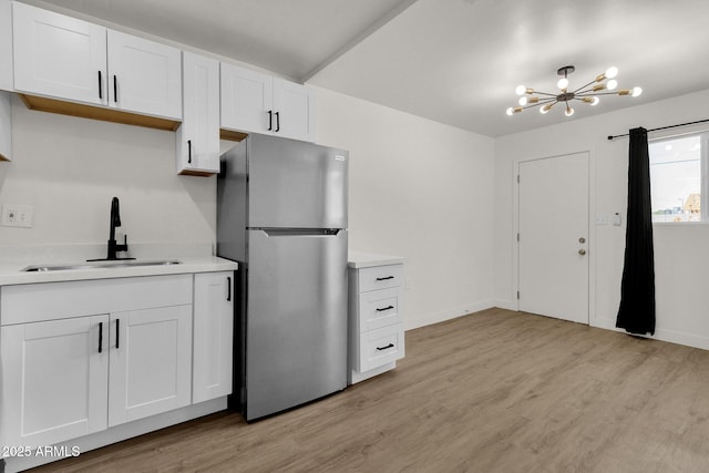 kitchen featuring white cabinets, sink, light hardwood / wood-style flooring, a notable chandelier, and stainless steel refrigerator