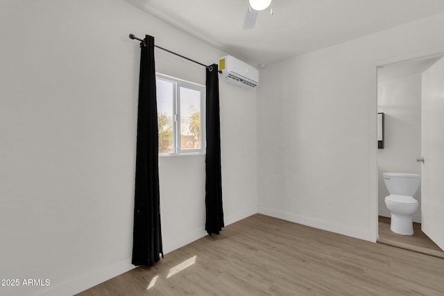 empty room with ceiling fan, a wall unit AC, and light hardwood / wood-style flooring