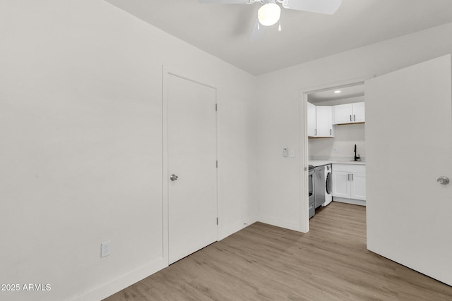 interior space featuring white cabinets, sink, ceiling fan, light wood-type flooring, and washer / dryer