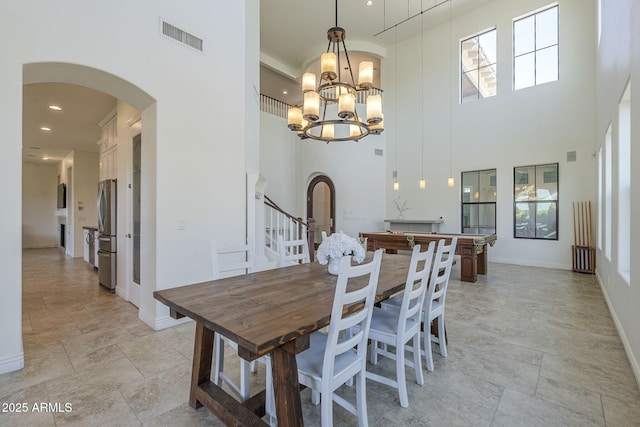 3812 E Camelback Rd, Phoenix, AZ 85018 - dining room featuring arched walkways, a towering ceiling, baseboards, a chandelier, and light stone finish flooring
