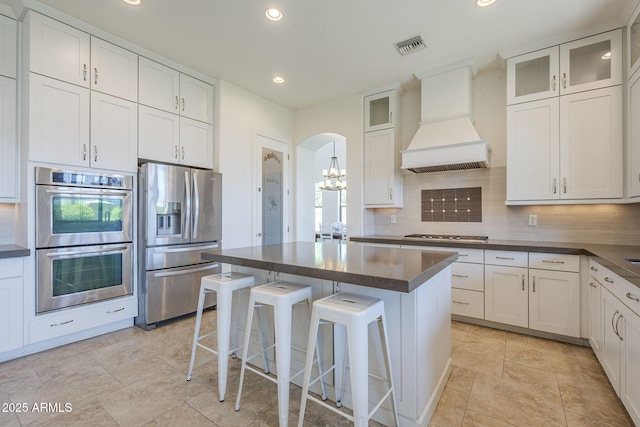 3812 E Camelback Rd, Phoenix, AZ 85018 - kitchen with stainless steel appliances, custom exhaust hood, dark countertops, tasteful backsplash, and arched walkways