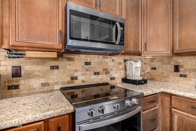 14819 W Lupine Ln, Surprise, AZ 85374 - kitchen featuring appliances with stainless steel finishes, backsplash, brown cabinetry, and light stone countertops