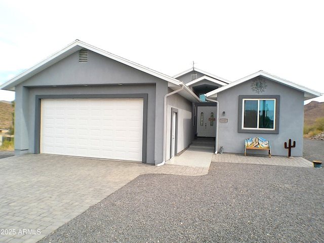 ranch-style house with a garage, decorative driveway, and stucco siding