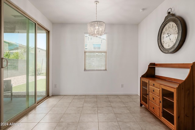 unfurnished dining area featuring plenty of natural light, a chandelier, light tile patterned flooring, and baseboards