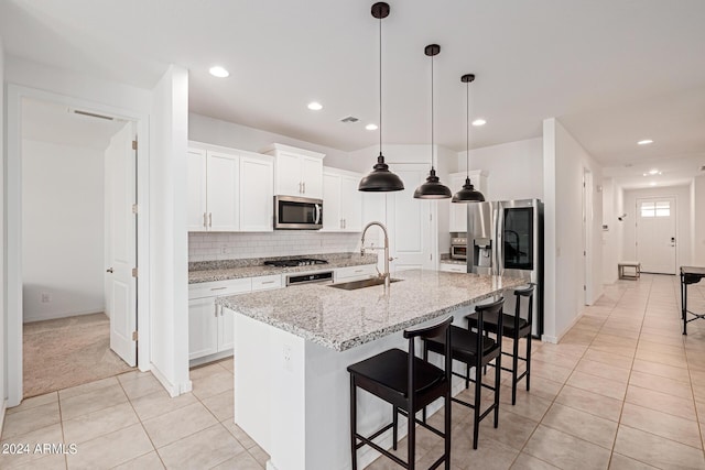 kitchen with a sink, appliances with stainless steel finishes, light tile patterned flooring, tasteful backsplash, and a center island with sink