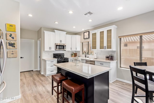 kitchen featuring stainless steel appliances, white cabinetry, light countertops, tasteful backsplash, and glass insert cabinets