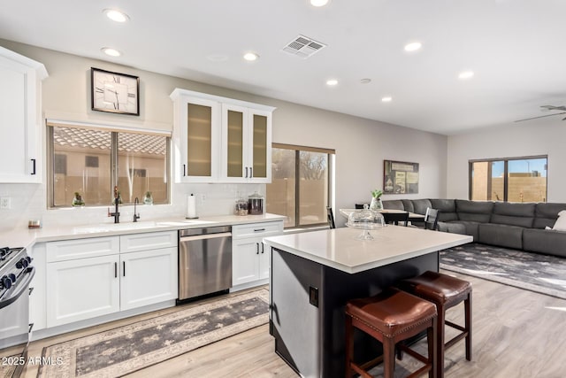 kitchen featuring a breakfast bar area, visible vents, stainless steel dishwasher, open floor plan, and white cabinetry