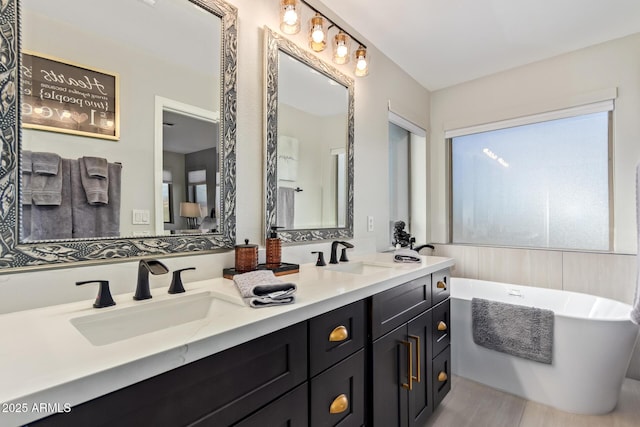 bathroom with double vanity, a freestanding tub, a sink, and wood finished floors