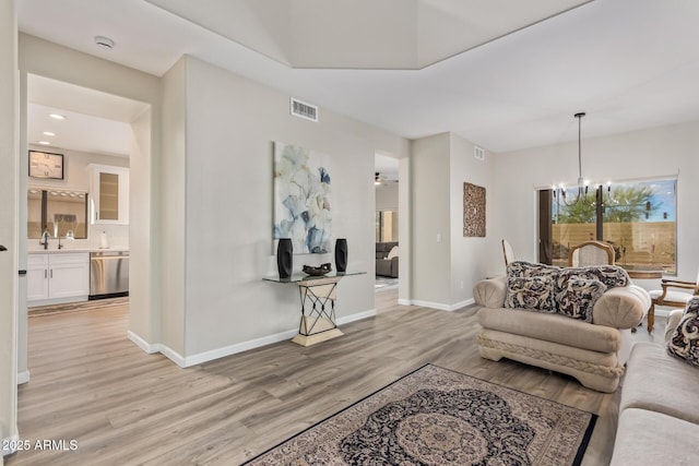 living area featuring light wood-type flooring, visible vents, baseboards, and an inviting chandelier