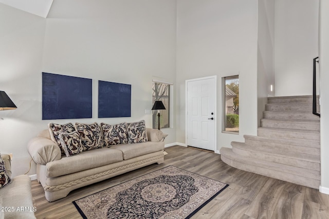 living room featuring stairway, wood finished floors, a towering ceiling, and baseboards