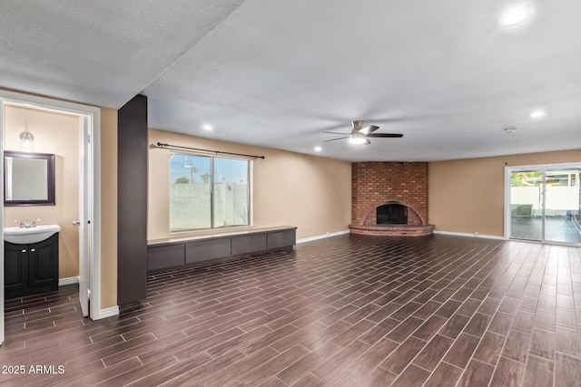 unfurnished living room with a textured ceiling, ceiling fan, sink, and a brick fireplace