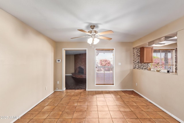 tiled spare room featuring plenty of natural light, ceiling fan, and a wood stove