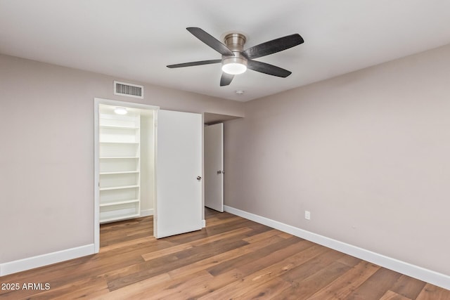 unfurnished bedroom with a walk in closet, ceiling fan, a closet, and light hardwood / wood-style floors