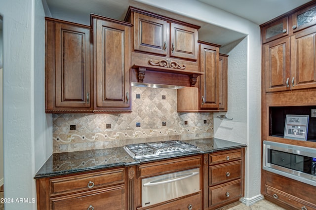 kitchen with appliances with stainless steel finishes, tasteful backsplash, custom exhaust hood, dark stone countertops, and light tile floors