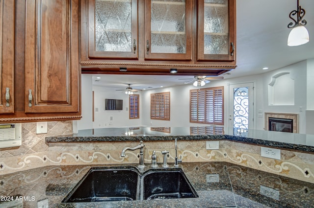 kitchen with backsplash, ceiling fan, dark stone counters, sink, and pendant lighting