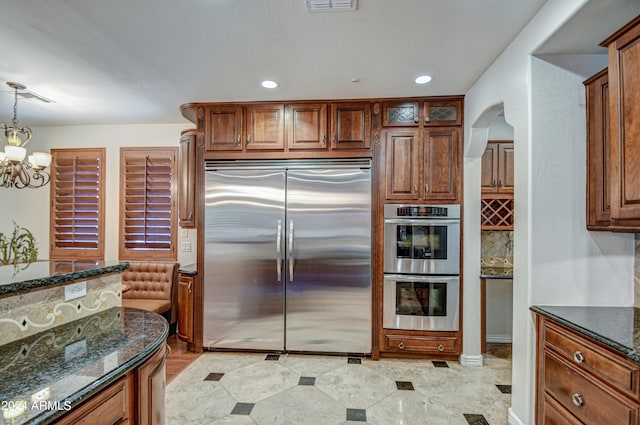 kitchen with backsplash, decorative light fixtures, a chandelier, stainless steel appliances, and dark stone countertops