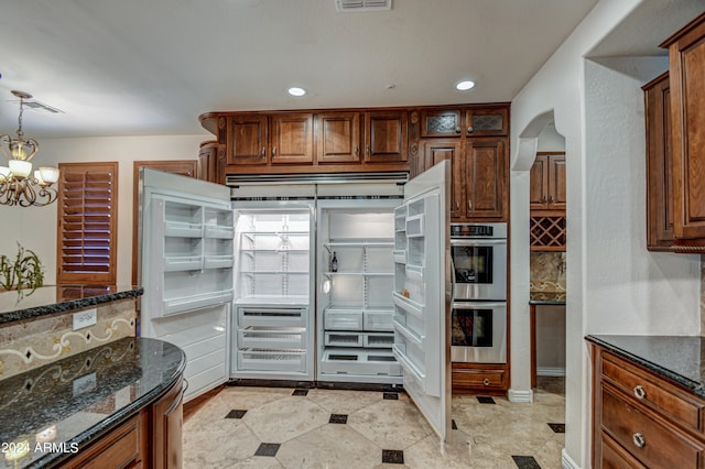 kitchen featuring stainless steel double oven, dark stone countertops, pendant lighting, and a chandelier