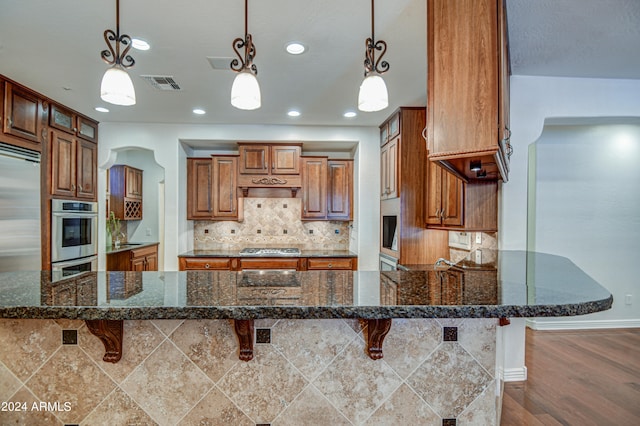 kitchen featuring a kitchen breakfast bar, hanging light fixtures, kitchen peninsula, hardwood / wood-style flooring, and dark stone countertops