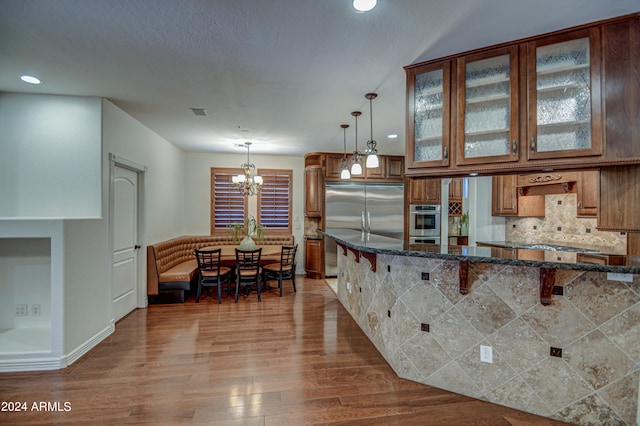 kitchen featuring tasteful backsplash, dark stone counters, hanging light fixtures, and hardwood / wood-style floors