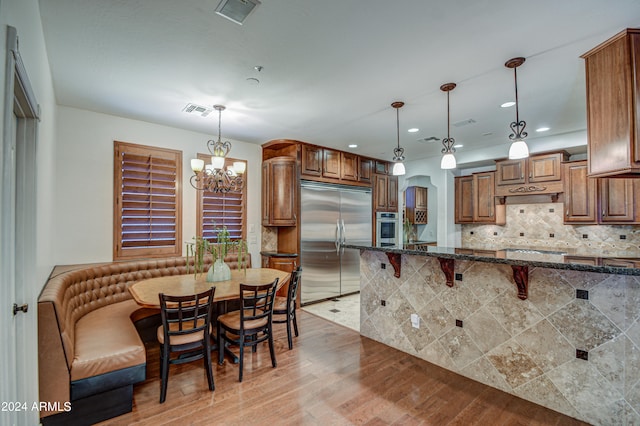 kitchen featuring backsplash, pendant lighting, stainless steel appliances, and light wood-type flooring