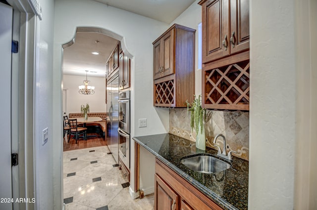 kitchen with decorative light fixtures, light wood-type flooring, backsplash, sink, and dark stone countertops