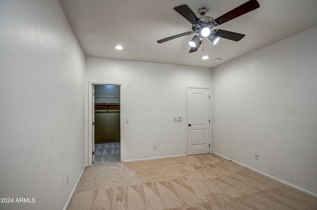 unfurnished bedroom with light colored carpet, a spacious closet, ceiling fan, and a closet