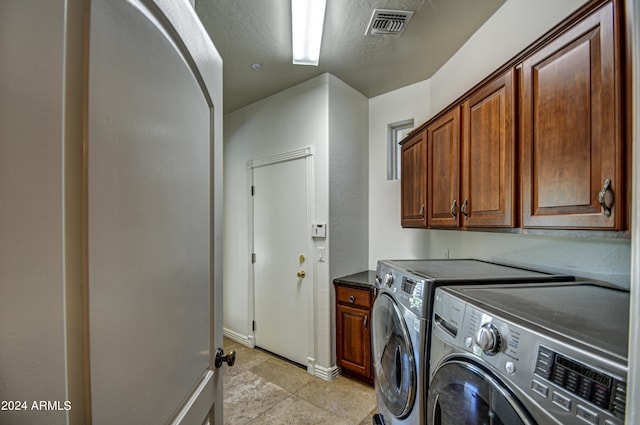 laundry room featuring washing machine and dryer, light tile flooring, and cabinets