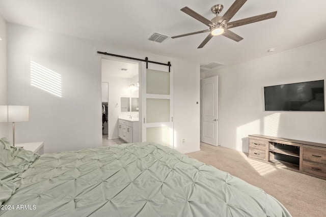 unfurnished bedroom with light carpet, a barn door, ensuite bath, and ceiling fan