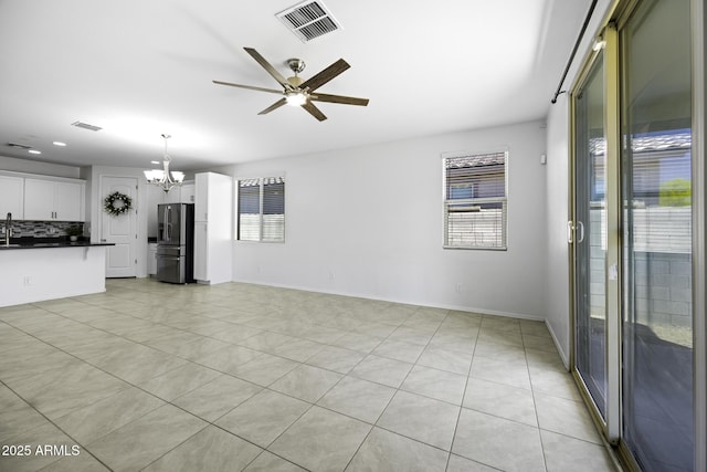 unfurnished living room featuring light tile patterned floors, a wealth of natural light, visible vents, and ceiling fan with notable chandelier
