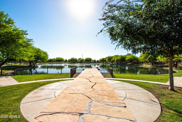 surrounding community featuring fence, a water view, and a lawn