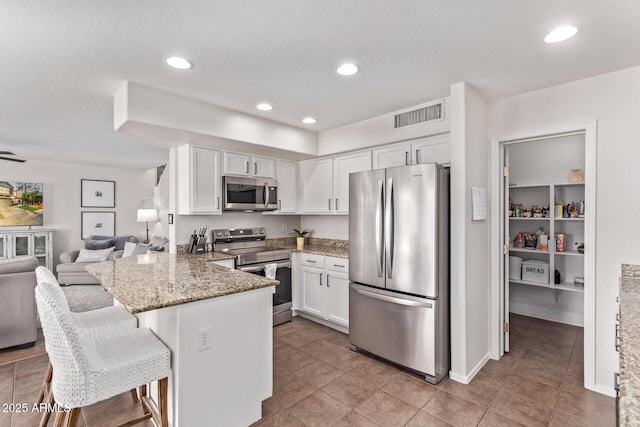 kitchen featuring appliances with stainless steel finishes, a breakfast bar, white cabinets, dark stone counters, and kitchen peninsula