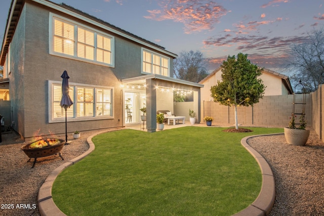 back house at dusk featuring a patio, a lawn, and a fire pit